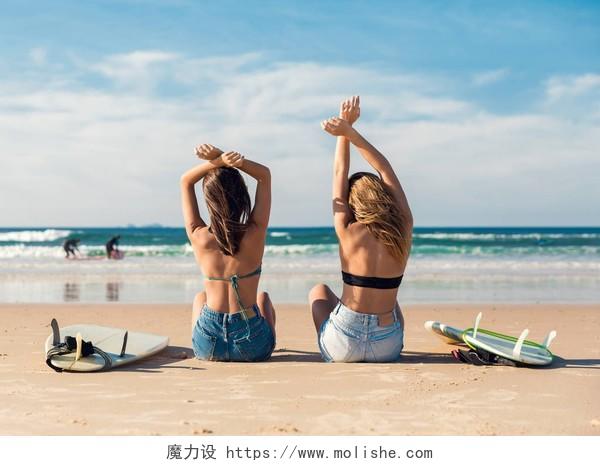 两个美丽的冲孩坐在沙滩上张开双臂